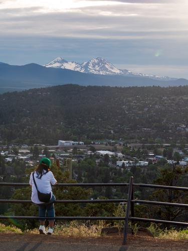 Подросток сидит на перилах и смотрит на горы (или в телефон)